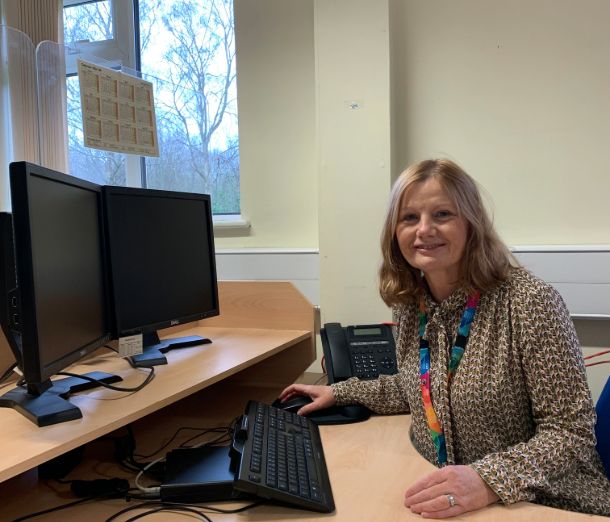 SWAP Course student, Amanda, sitting at a computer and smiling at the camera, wearing an NHS lanyard