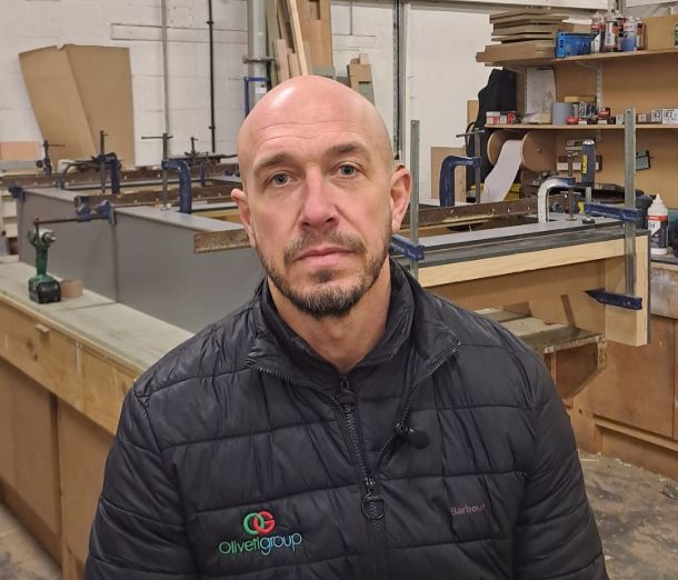 Director of Oliveti, Gareth Smith, standing in a workshop wearing a company branded dark jacket