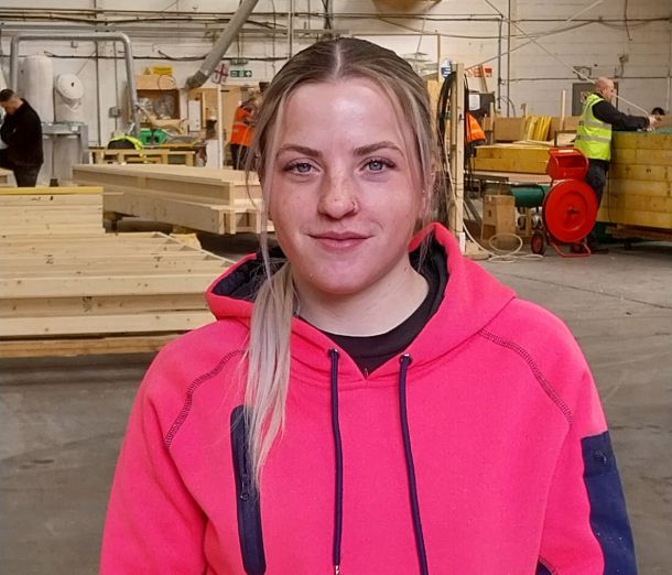 Former Leicester College student, Lana Craxford, standing in a workshop wearing a bright pink hoodie