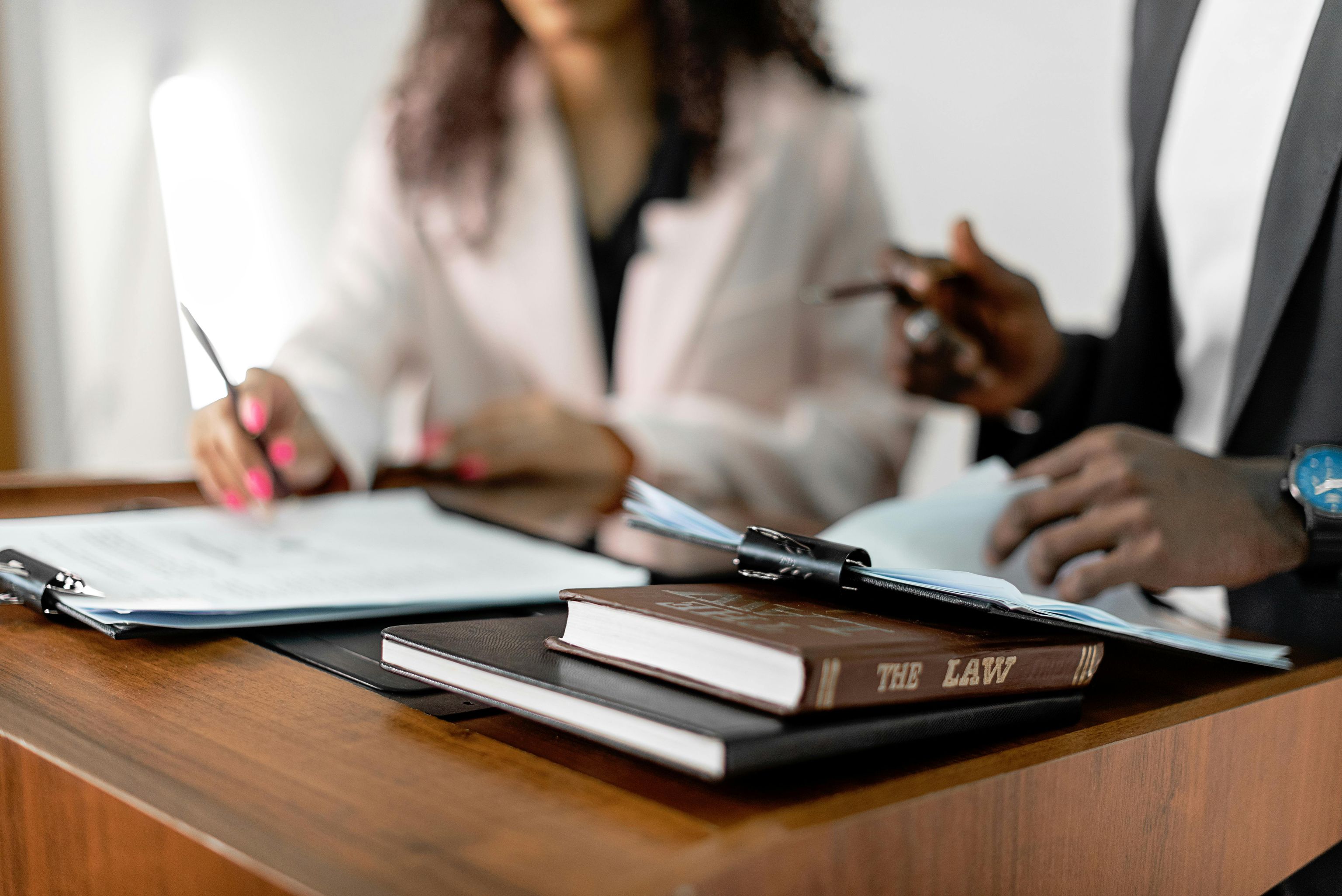 Stock image of a female and male discussing a topic with law books in front of them.