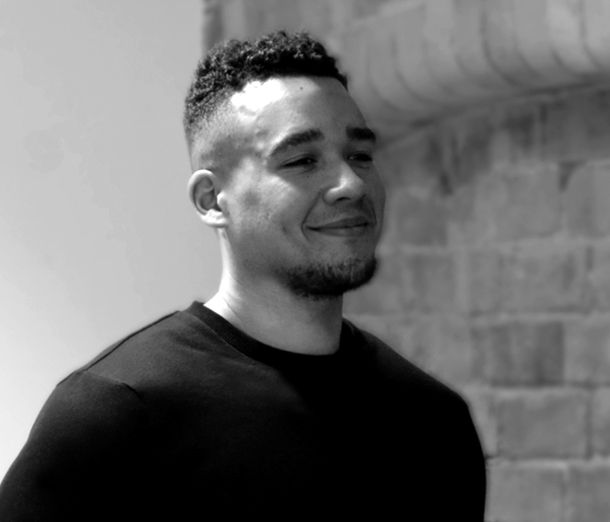 Leicester College student Liam, wearing all black and smiling while standing side on to the camera