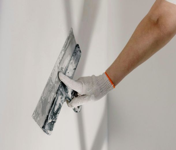 Image of a gloved hand applying plaster to a white wall using a plastering trowel