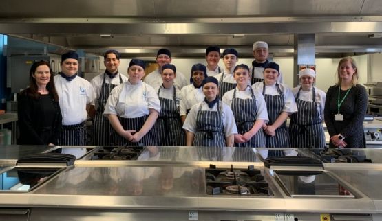 Group shot of Leicester College catering students with guests in a professional kitchen