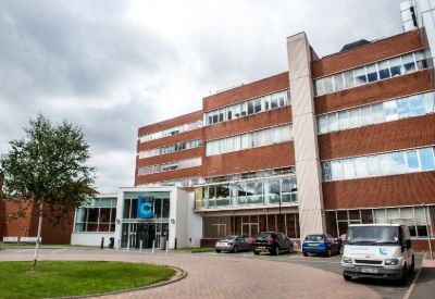 Image of the front of Leicester College's Freemens park campus - a large brick building with the college's logo on the front and vehicles parked outside