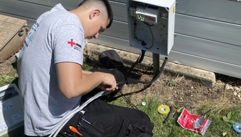 Leicester College apprentice crouched down outside of a property, working on wiring