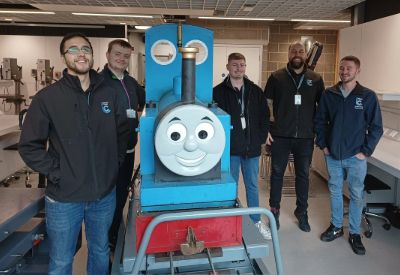 Leicester College T Level students standing with a model of Thomas the Tank engine in a workshop