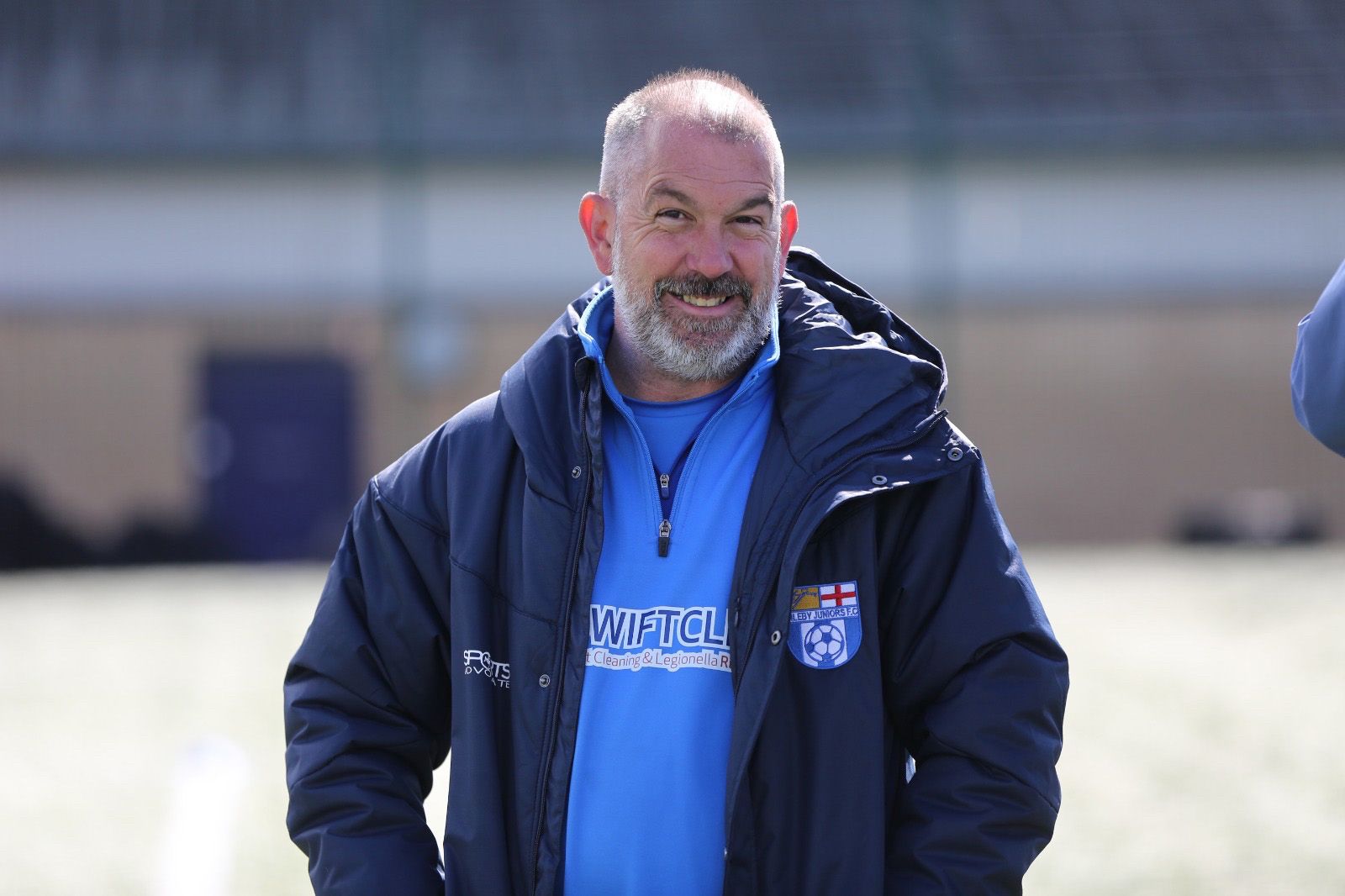 picture of james in a jacket smiling at camera - white male with grey hair and grey and dark brown beard.