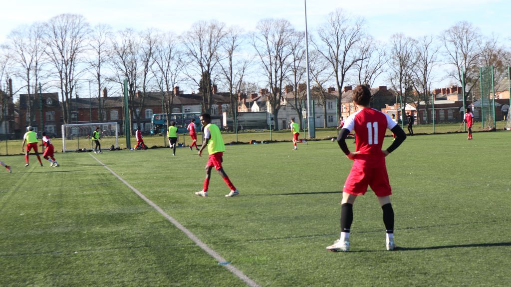 men playing football outdoors on a pitch, a person in the foreground with a red kit and number 11 on the back of his shirt.