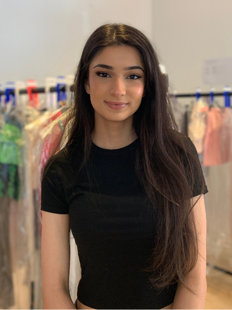 student with long dark hair standing in front of a fashion rail