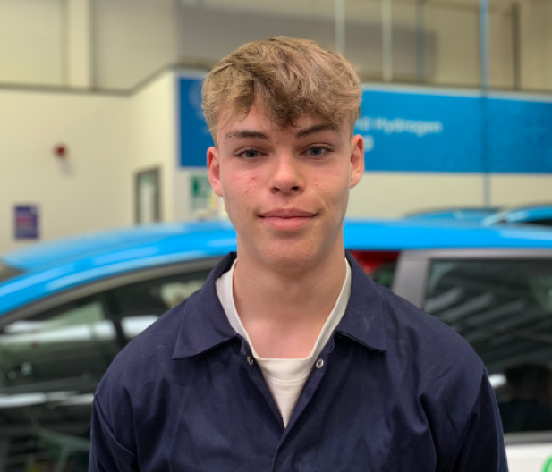 student in motor vehicle workshop wearing blue overalls