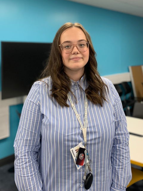 Chelsea in a striped shirt stood in a classroom